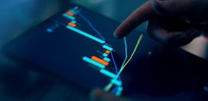 A hand pointing at a colorful trading chart on a tablet screen in a dimly lit environment.