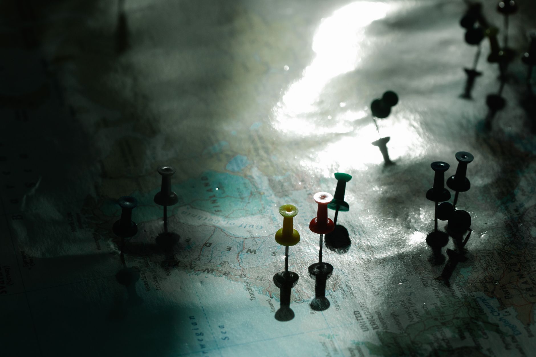 Close-up of colorful pushpins on a map, highlighting specific locations, with soft lighting and shadows.